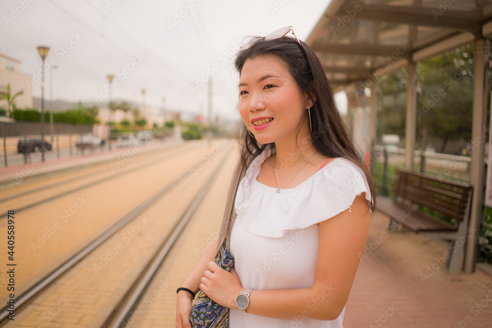 young beautiful Asian woman waiting for train - lifestyle portrait of attractive and happy Chinese girl at railway platform waiting relaxed in transport concept