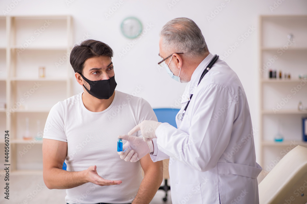 Fototapeta premium Young male patient visiting old doctor in vaccination concept