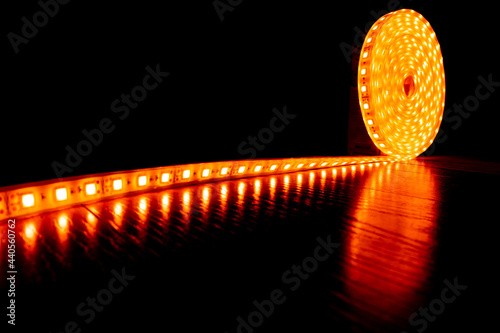 diode decorative tape for lighting, a roll of LED strip with yellow warm light on the floor laminate.