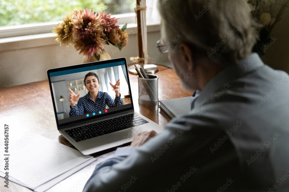 Back view of old Caucasian man look at laptop screen talk speak on video  call with