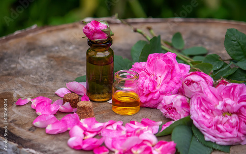 Close-up of rose essential oil bottle with falling leaves on wooden background.