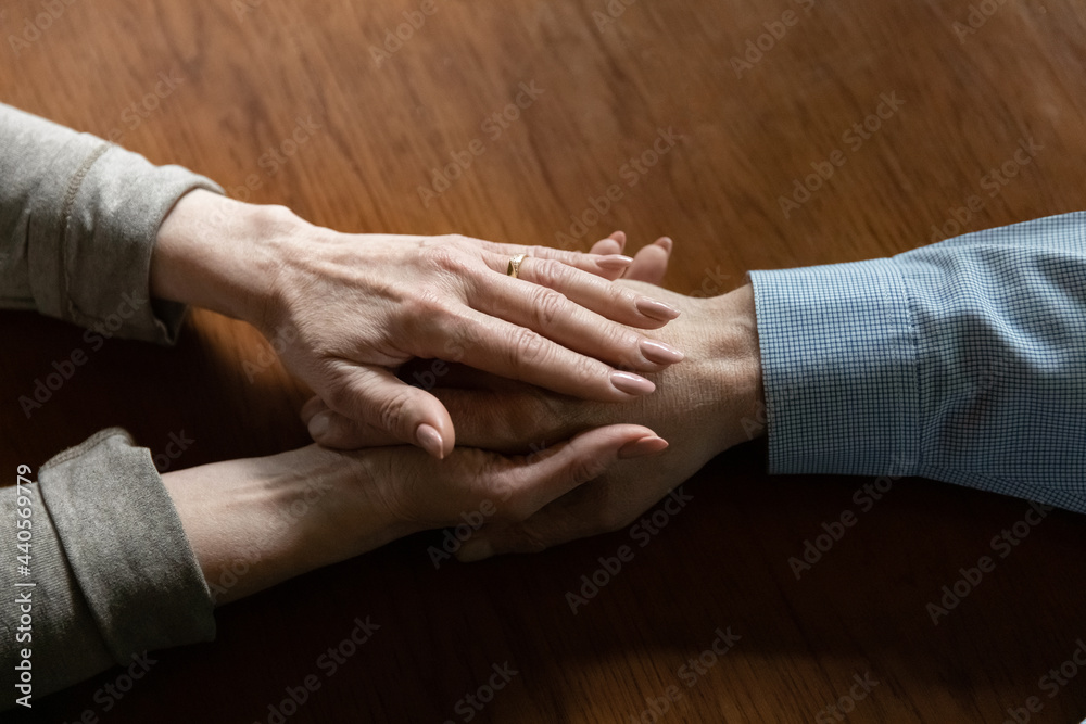 Fototapeta premium Crop close up of mature woman hold old husband hand show love and care in relationships. Attentive middle-aged wife comfort caress support senior man spouse, feel supportive. Family unity concept.