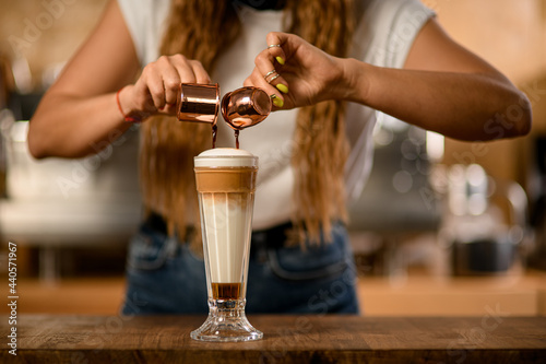 glass with syrup and whipped cream into which barista pours espresso from cups