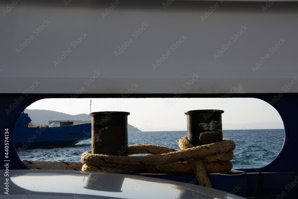 Close-up  of the bollards on a ship with ropes tied on them, beautiful calm water and ship in front