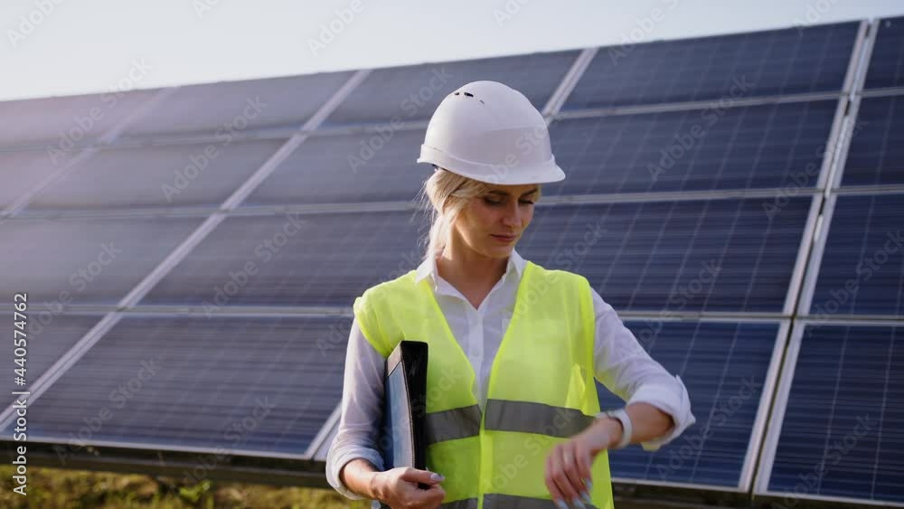 Portrait of beautiful female engineer technologist standing among solar panels. Woman in protective helmet and uniform smiling at camera Portrait of beautiful female engineer technologist standing among solar panels. Woman in protective helmet and uniform smiling at camera