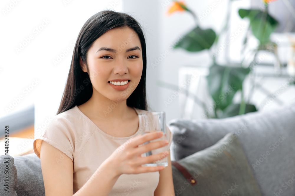 Healthy lifestyle concept. Positive, pretty chinese or japanese young woman in a t-shirt, holds a glass of clean water, looks at the camera, smiles, cares of her health, drinks the daily norm of water