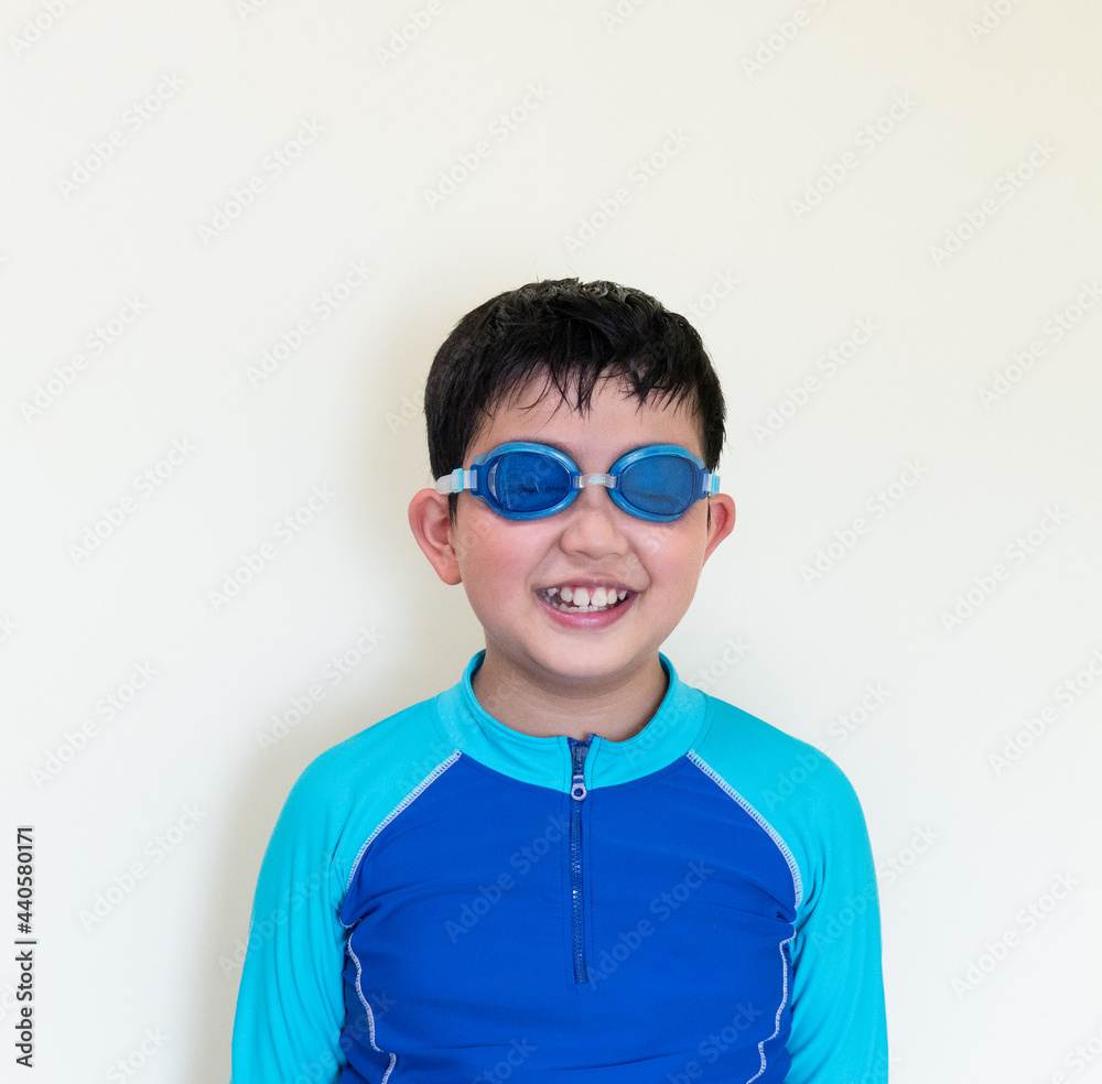 Portrait of little young boy in the blue swimsuit and goggles isolated on plain background.The happy smiling Asian kid and the swimming activity concept. Portrait of little young boy in the blue swimsuit and goggles isolated on plain background.The happy smiling Asian kid and the swimming activity concept.