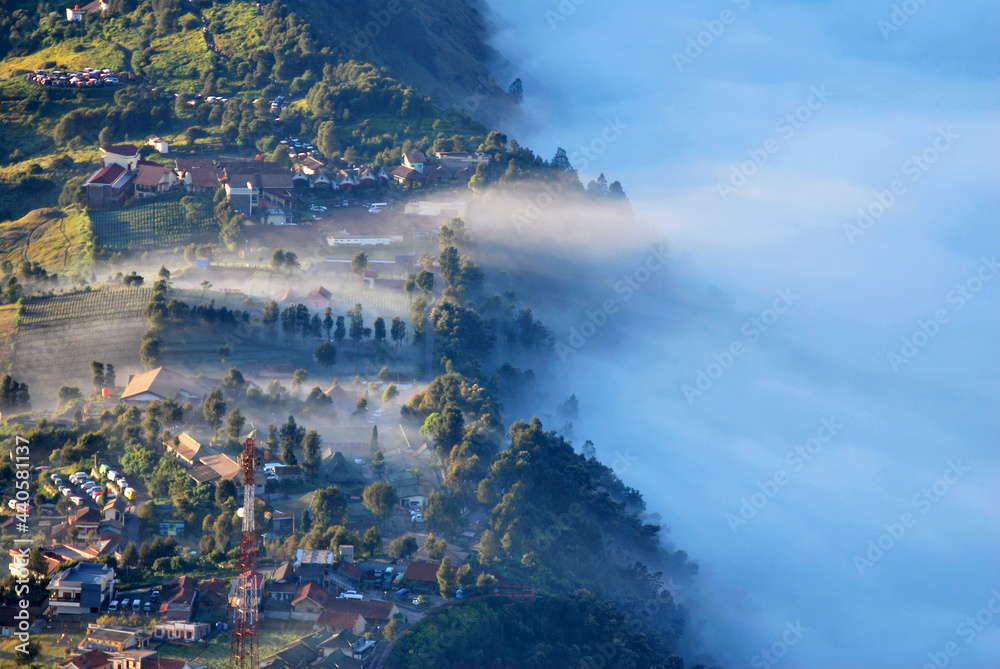 Landscape natural scene of Little village with many fog and Misty around mountain and village with shining sunrise at cemero lawang of Bromo Mountain , Indonesia - Morning vibe greenery travel unseen