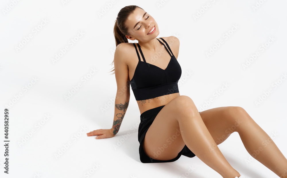 Female athlete in sports clothing, resting on floor after workout jogging, isolated on white background. Sportswoman sitting in activewear with pleased smile, finish exercise training