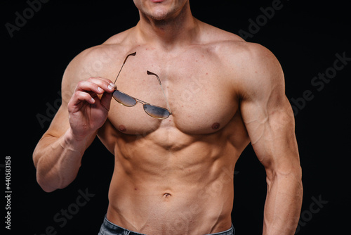A young sexy athlete with perfect abs poses in the studio topless in jeans in a pair of protective glasses. Healthy lifestyle, proper nutrition, training programs and nutrition for weight loss.