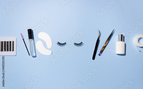 Tools for eyelash extension on a blue background. Artificial eyelashes, self-care. Tweezers, glue, and other tools for lashmaker work. Top view, copyspace.