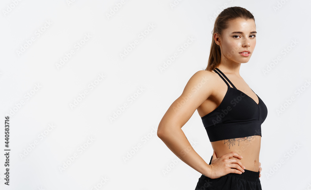 Fototapeta premium Confident healthy and athletic woman staring determined at camera, holding hands on hips. Sportswoman exercising in sport clothing, training and workout on white background, isolated