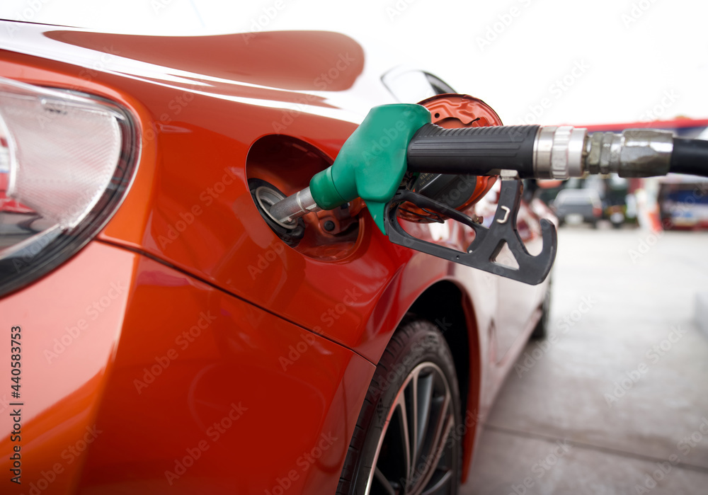 Green benzene gas pump nozzle filling up red sport car tank. Close up