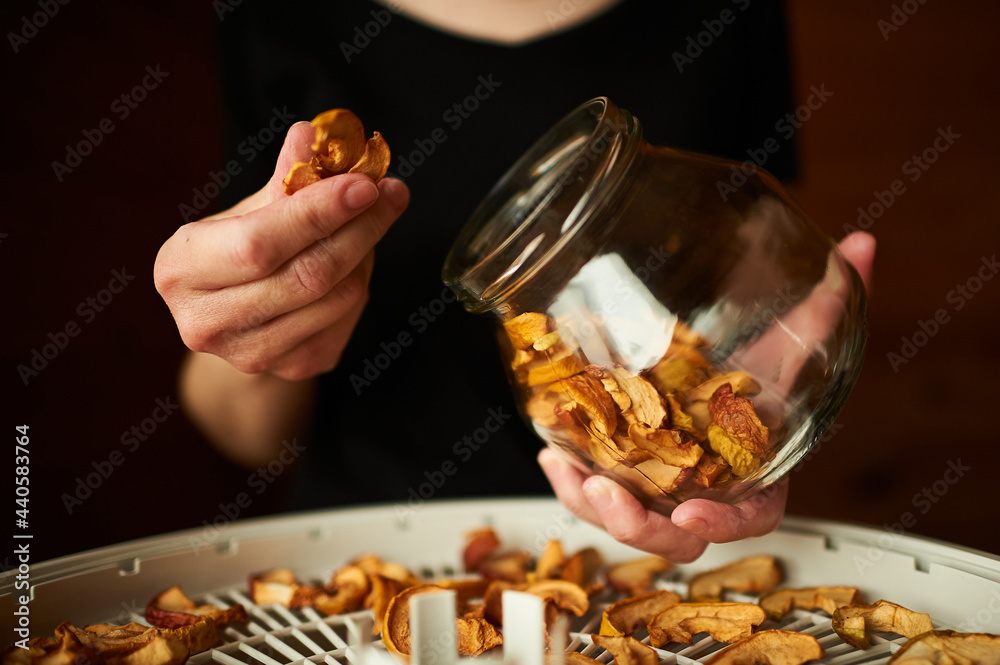 A woman's hands are filling the glass jar all the way to the top with dried apple chunks. A food dried in order to be used in food and desserts for the winter. Drying food in a dehydrator. A woman's hands are filling the glass jar all the way to the top with dried apple chunks. A food dried in order to be used in food and desserts for the winter. Drying food in a dehydrator.