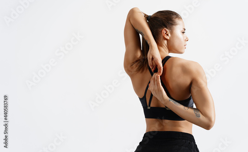 Rear view of fit and sporty fitness woman stretching arms and back before workout exercises. Woman back in black sport clothing standing on white background, training concept