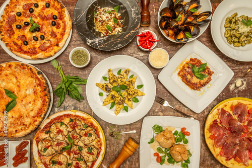 Top view image of typical Italian dishes with lots of basil, pizzas, pasta, gnocchi, tomatoes and vegetables
