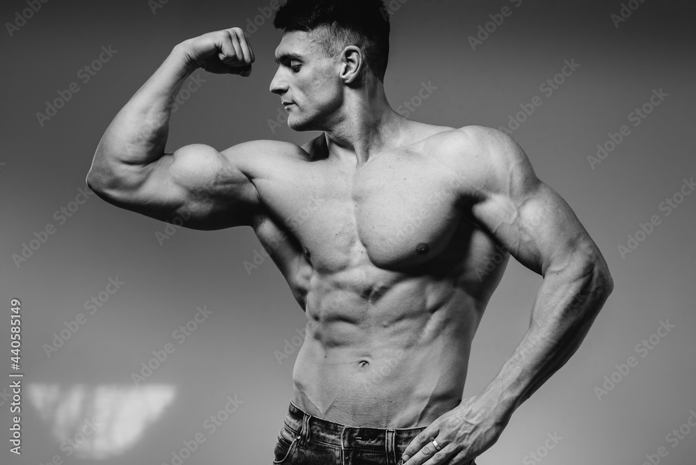 A young sexy athlete with perfect abs poses in the studio topless in jeans. Healthy lifestyle, proper nutrition, training programs and nutrition for weight loss. Black and white.