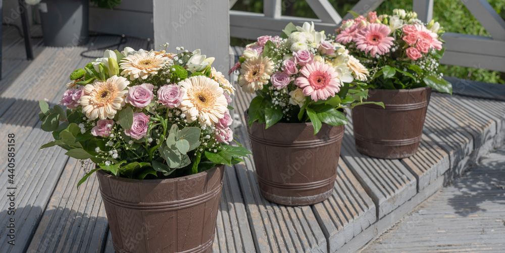 Three brown flower pots with bouquets of flowers.