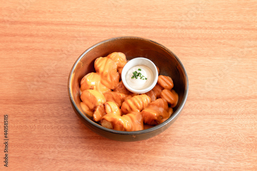 Fantastic portion of patatas bravas a la Madrid with spicy sauce and mayonnaise with chopped chives on a cherry wood table