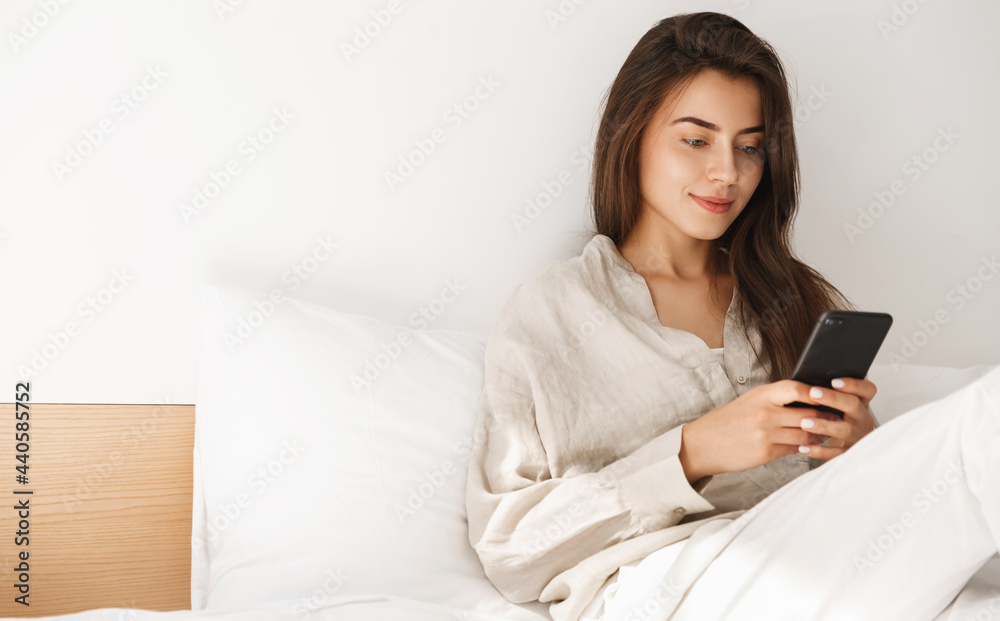 Young woman lying in bed with smartphone. Girl chatting on mobile phone from her bedroom, resting and browsing internet, scrolling entertainment app Young woman lying in bed with smartphone. Girl chatting on mobile phone from her bedroom, resting and browsing internet, scrolling entertainment app