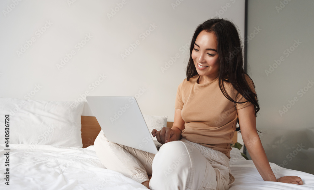 Image of young asian woman using computer in bed. Smiling girl watching video on laptop in her bedroom, e-learning or browsing internet websites, online shopping at home Image of young asian woman using computer in bed. Smiling girl watching video on laptop in her bedroom, e-learning or browsing internet websites, online shopping at home