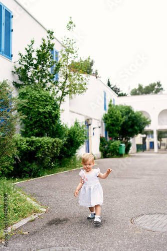Little girl walks on the asphalt in the yard of the house © Nadtochiy
