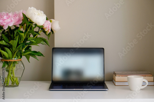 Home office concept. Designated work from home area near the window. Modern laptop  notebook and vase with flowers on table. Close up  copy space  background.