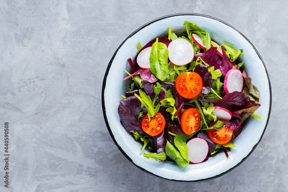 Salad with mix of greens on gray background. Healthy vegetable salad with cherry tomatoes, radish and mix salad. Copy space Salad with mix of greens on gray background. Healthy vegetable salad with cherry tomatoes, radish and mix salad. Copy space