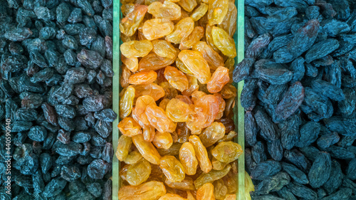 Close up three varieties of raisins piled up for fruit and vegetable shop window. Different types of dry grapes, light small, dark, blue large raisins. Selective focus, horizontal banner photo