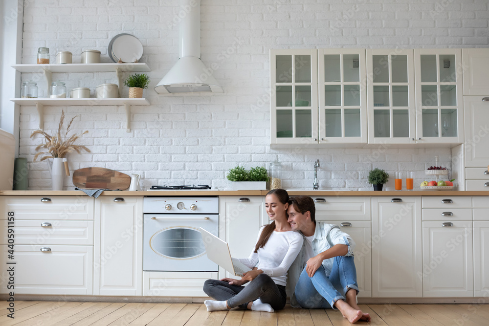Cheerful couple with laptop make a choice in the online store sitting on the kitchen floor. Cheerful couple with laptop make a choice in the online store sitting on the kitchen floor.