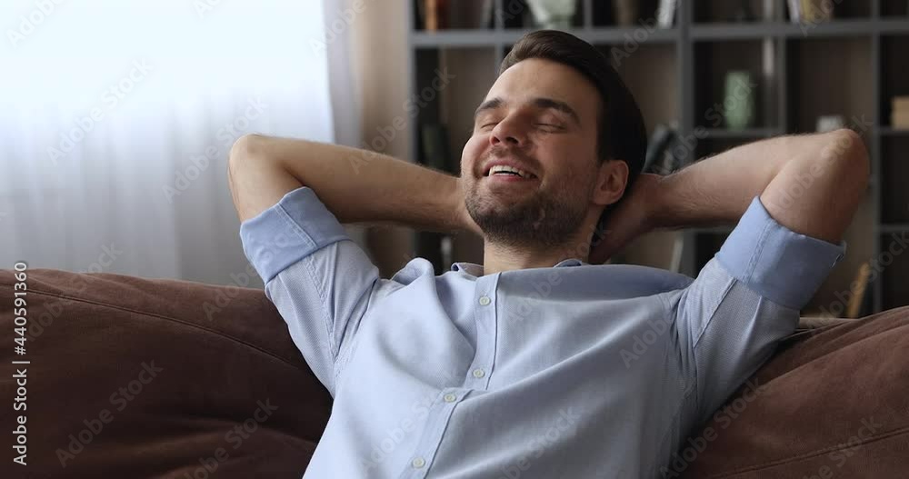 Close up serene calm millennial smiling man put hands behind head lean on comfy sofa resting alone at home, feel satisfaction enjoy fresh conditioned air inside of cozy living room, relaxation concept Close up serene calm millennial smiling man put hands behind head lean on comfy sofa resting alone at home, feel satisfaction enjoy fresh conditioned air inside of cozy living room, relaxation concept