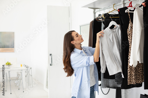 Attractive woman standing near hangers with clothes, thinking what to dress for a business meeting with comrades.