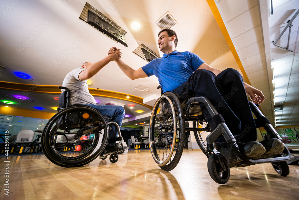 Obraz premium Two young disabled men in wheelchairs playing bowling in the club