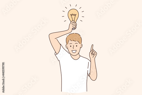 Having business idea and innovation concept. Young caucasian positive man cartoon character standing with light bulb above feeling excited vector illustration 