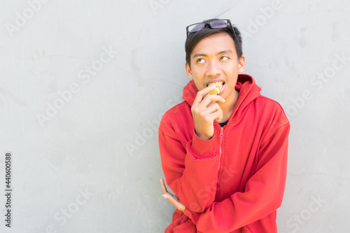 Indonesian guy with a red jacket eating a piece of cake and thinkin on a white background photo