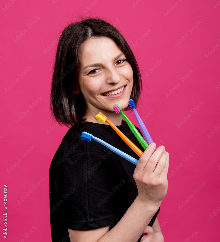 Beautiful happy young woman with different colored toothbrushes on blank pink background