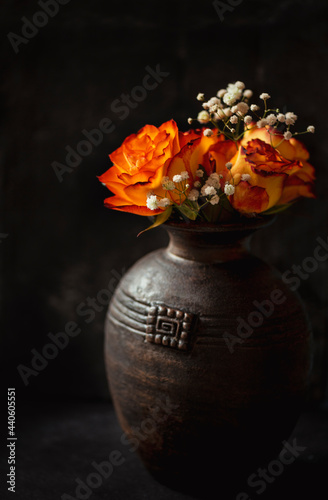 Vintage vase with orange roses flowers made in studio on low key stile dark mood 