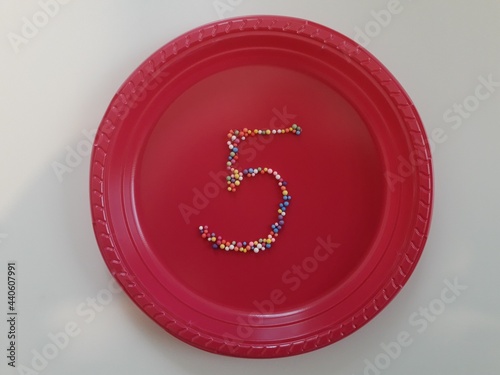 Number 5 in colouful confetti on pink paper plate 
