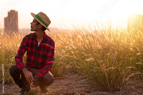Farmer with hat in farm plantation on sunset. Buildings and city blurred background. Space for text.
