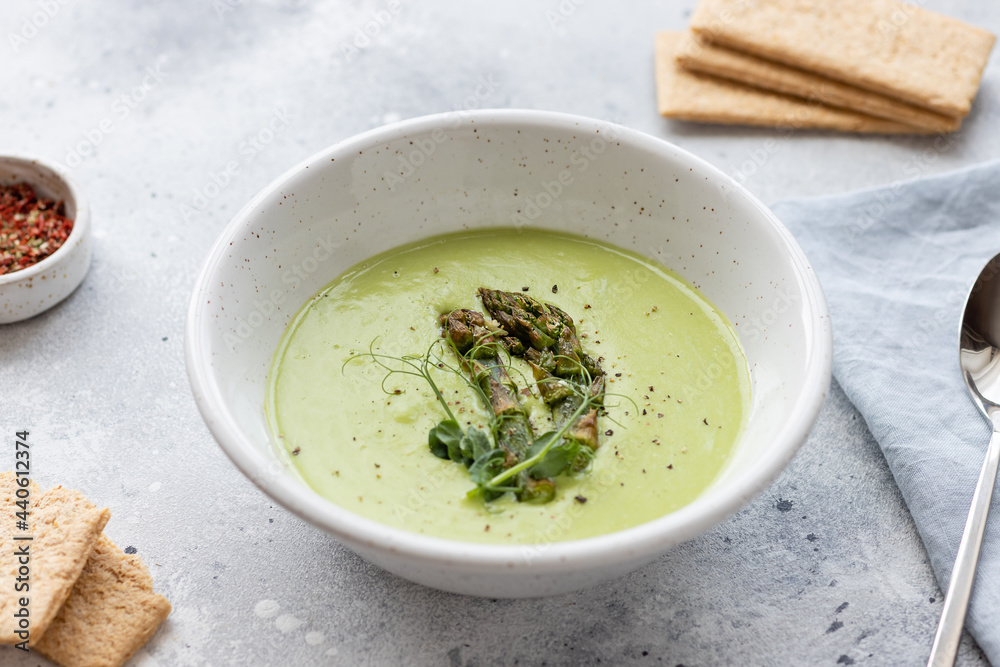 asparagus cream soup in ceramic bowl and rice crackers on gray table. Vegan, diet food asparagus cream soup in ceramic bowl and rice crackers on gray table. Vegan, diet food