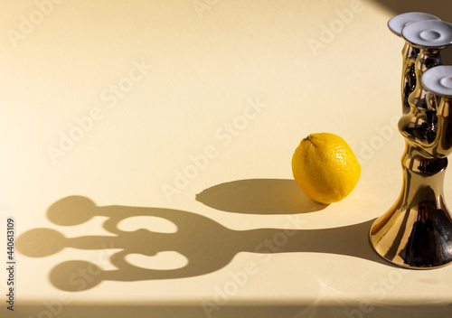 beautiful trident shape shadow from a golden candlestick on a beige background, a composition of lemon and a vintage candelabrum under hard light, long glitter geometric shadows, copy space