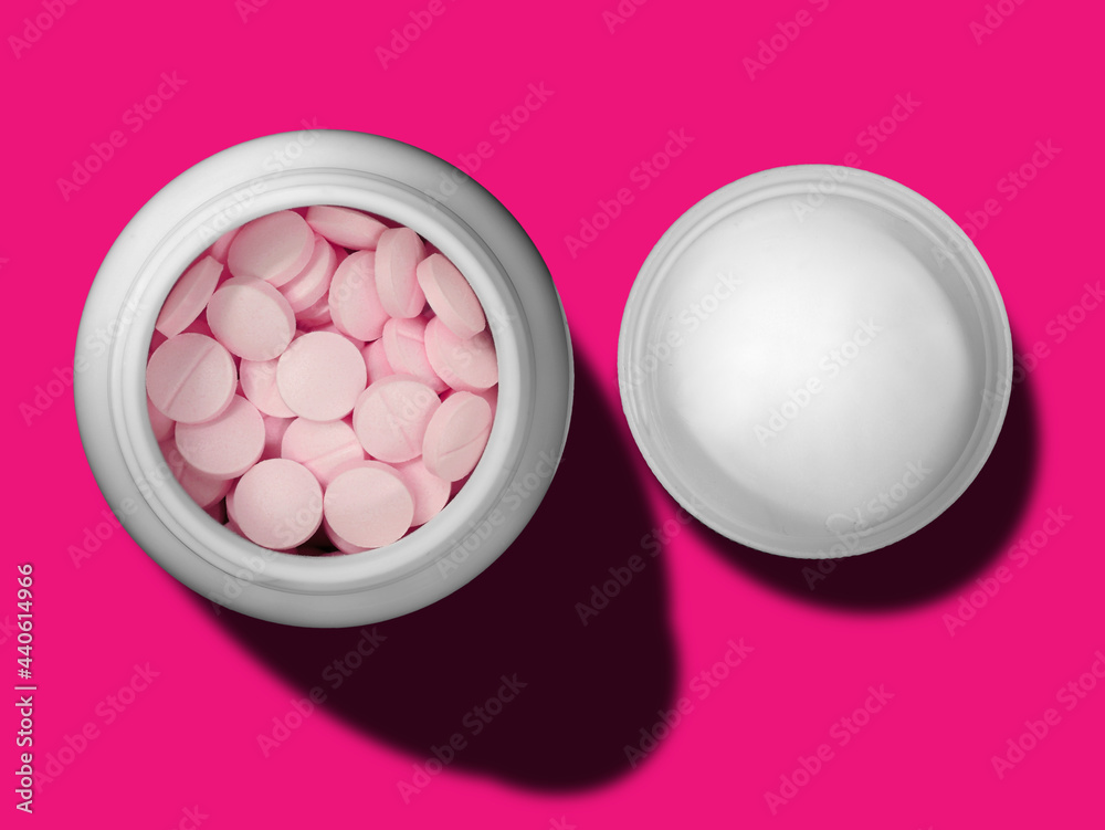 top view of pink pills in white bottle and cap on magenta background top view of pink pills in white bottle and cap on magenta background
