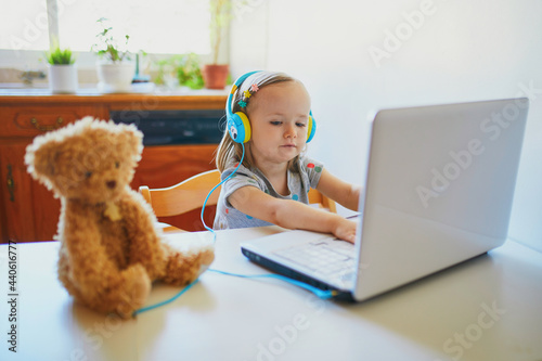 Toddler girl wearing eraphones with laptop photo