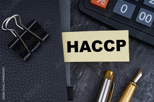 On the table is a calculator, a pen and a notebook with a bookmark on which it is written - HACCP