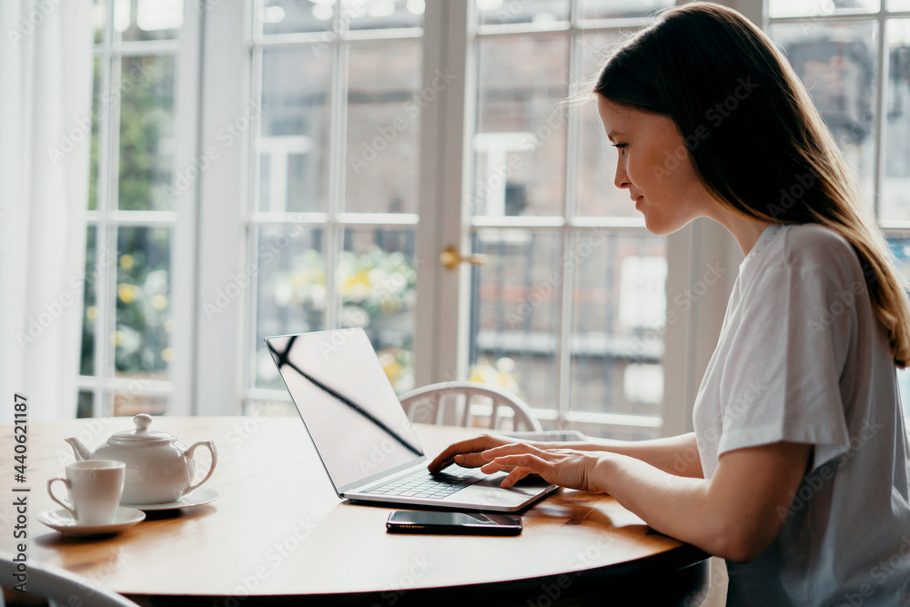 Surfs the Internet looking for purchases on the site. Young female freelance student working at home on a laptop. Distance learning in the apartment. Surfs the Internet looking for purchases on the site. Young female freelance student working at home on a laptop. Distance learning in the apartment.