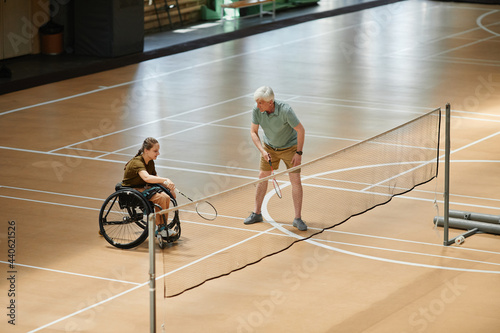 Wide angle view at young sportswoman in wheelchair playing badminton during practice at indoor court, copy space