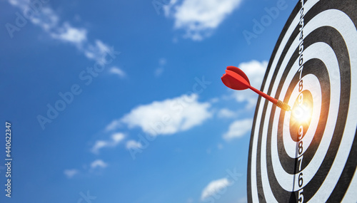 Red dart target arrow hitting on bullseye with blue sky and sunlight. Dreaming for target marketing and business success concept. Scoreboard defining clear goals.