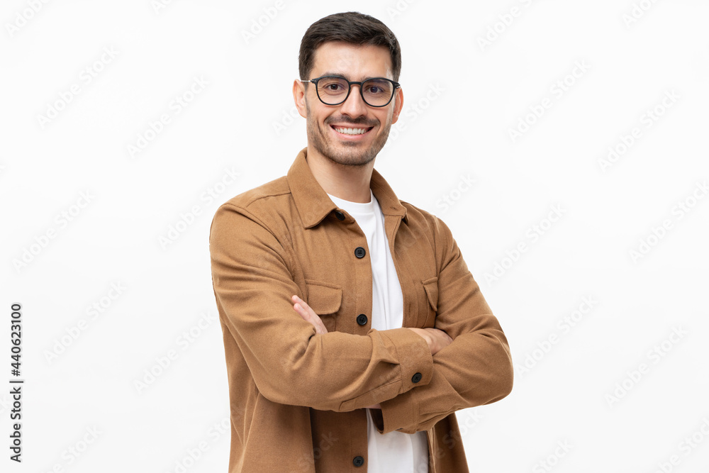 © Damir Khabirov - Young hispanic man wearing brown shirt and glasses, looking at camera with positive confident smile, holding arms crossed, isolated on gray background