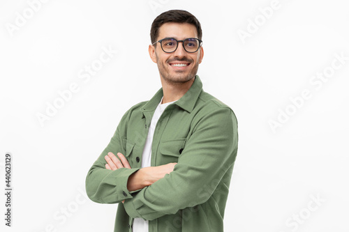 Confident young man in casual green shirt looking away, standing with crossed arms isolated on gray