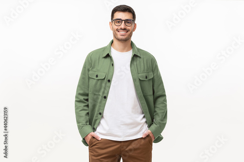 Young man standing with hands in pockets, wearing casual green shirt, looking at camera, isolated on gray background